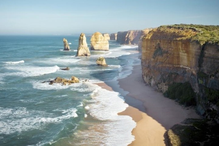 a close up of a rock next to a body of water with The Twelve Apostles in the background